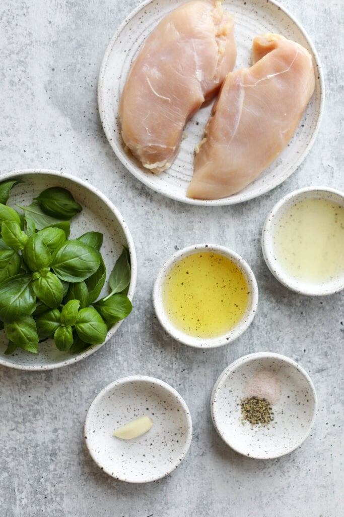 Overhead view of all ingredients for basil pesto chicken marinade arranged together in small bowls and plates. 