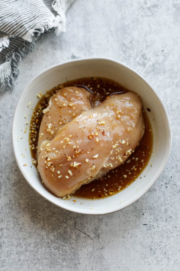 Overhead view of two chicken breasts in honey garlic chicken marinade in bowl.