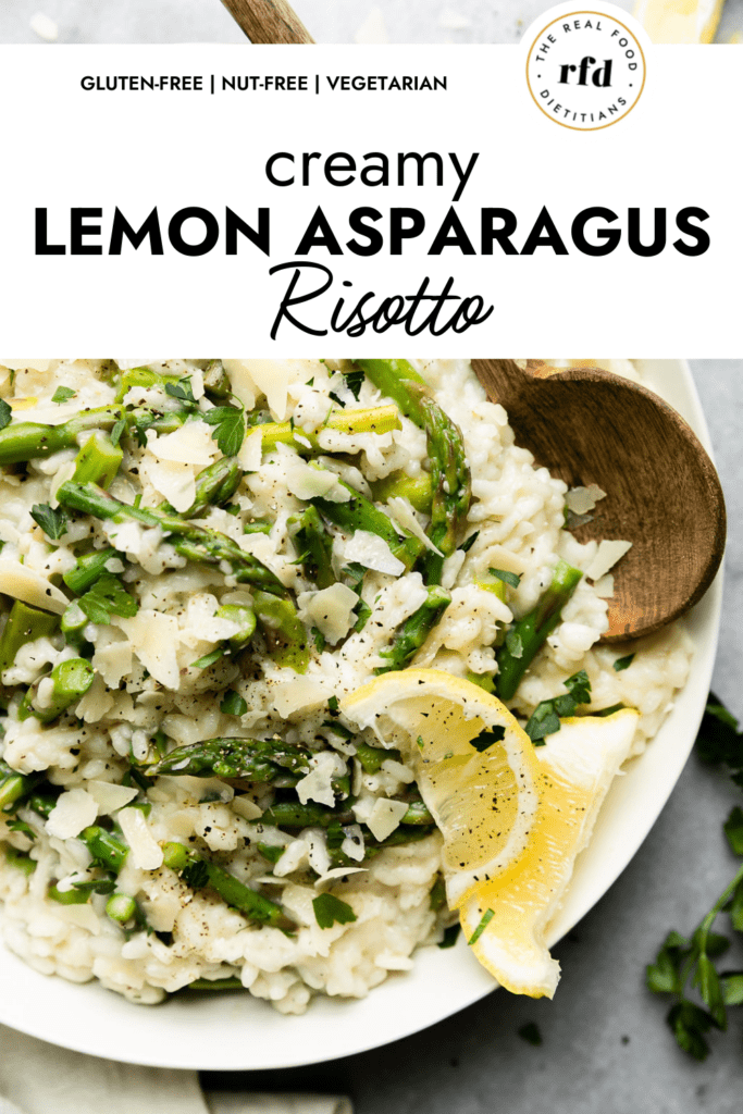 Close up view of lemon asparagus risotto in a white bowl topped with cracked black pepper and lemon wedges, a wooden spoon on the side. 