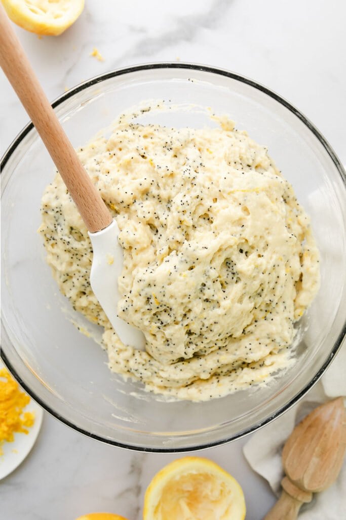 Overhead view of lemon poppy seed muffin batter in a clear bowl with a white spatula in batter. 