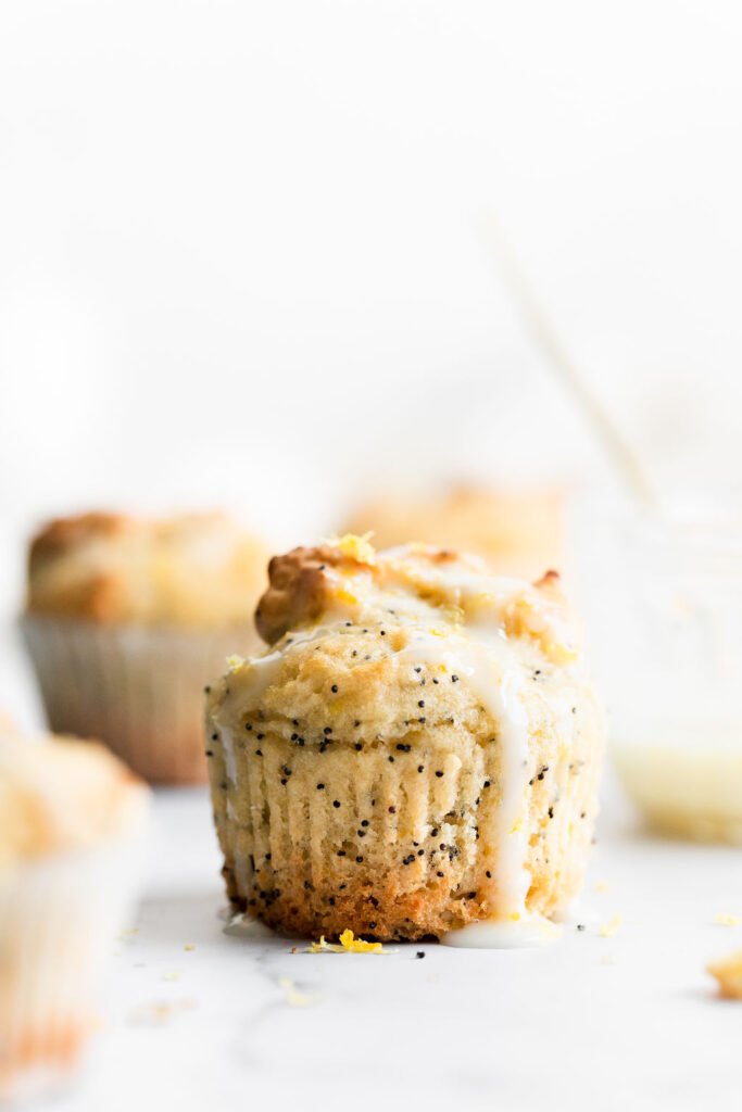 A close up side view of a lemon poppy seed muffin on a white countertop with lemon glaze sliding the sides. 