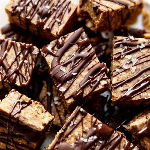 Overhead view of mini peanut butter protein bars in a pile, drizzled with dark chocolate and sprinkled with sea salt flakes.