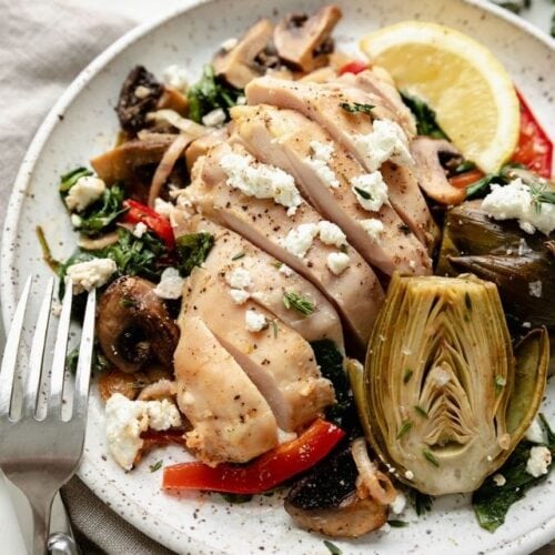 Sheet pan artichoke chicken served on a plate with chicken cut into strips, roasted baby artichokes, and topped with goat cheese.