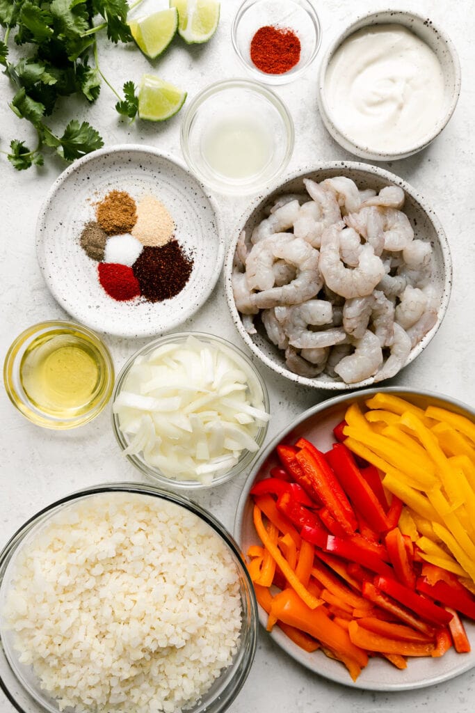 Overhead view of all ingredients for shrimp fajita bowls arranged in small bowls and plates. 