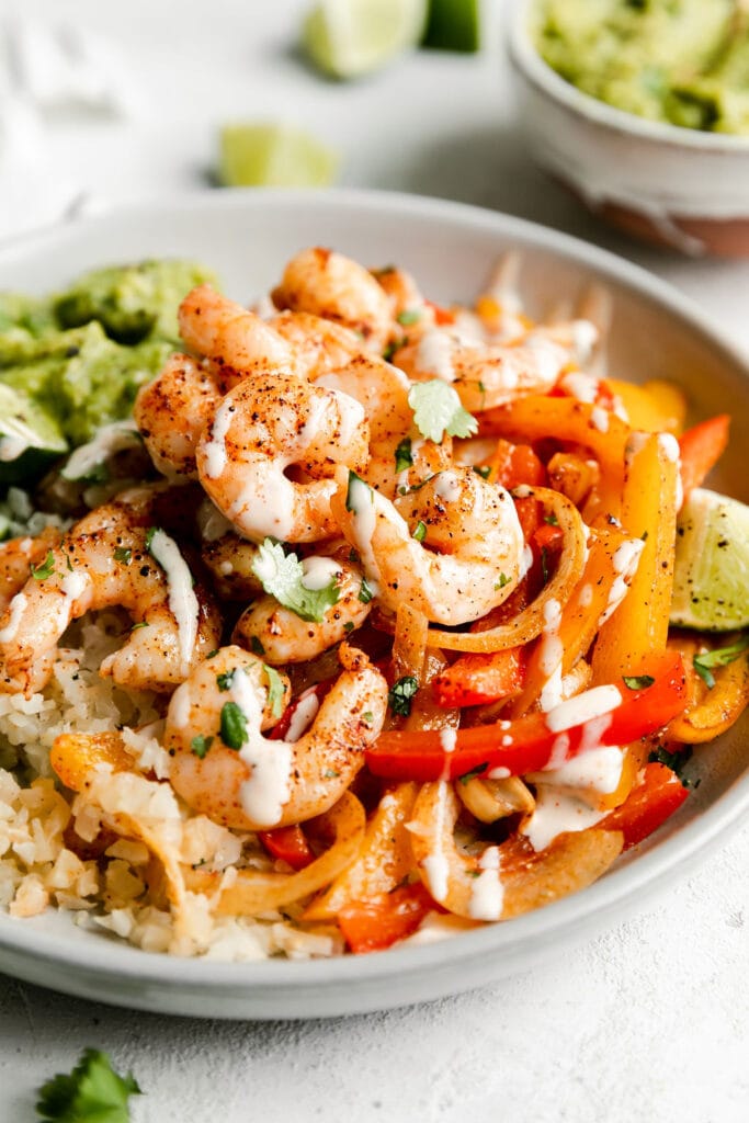 Sheet pan shrimp fajita bowls served in shallow bowl topped with seasoned shrimp and drizzled with ranch