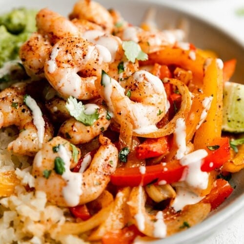 Close up view of sheet pan shrimp fajitas served in a bowl topped with sauce.