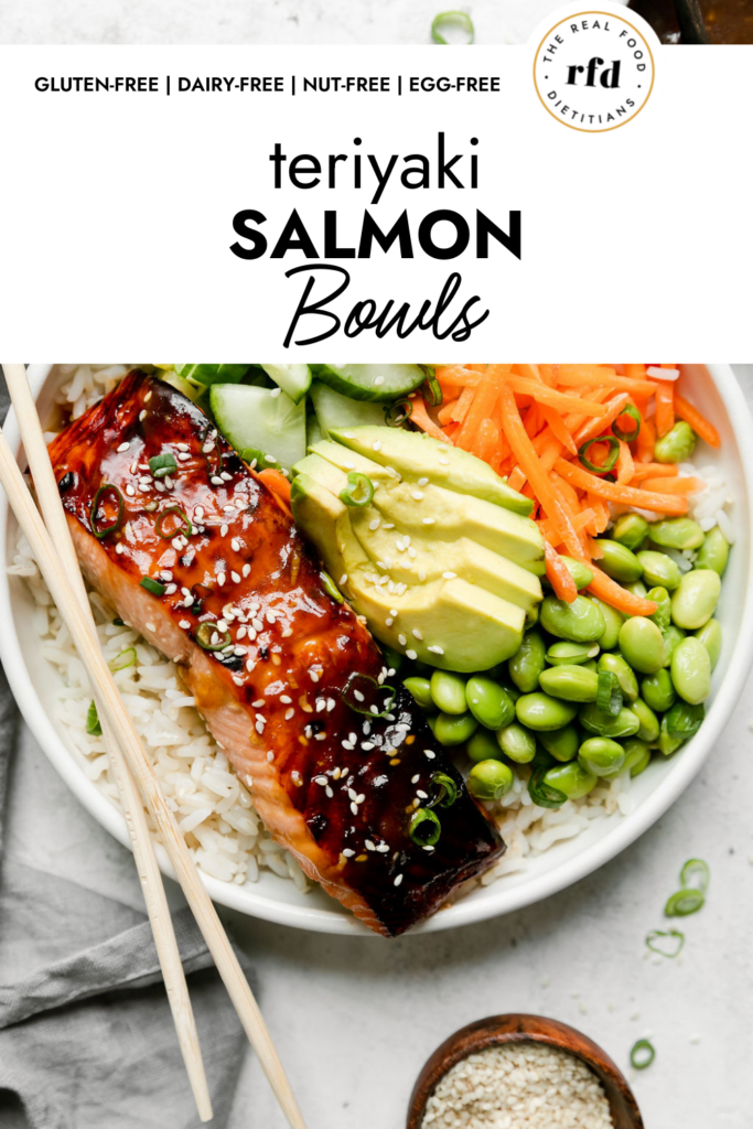Teriyaki Salmon Bowl served in a white bowl over white rice topped with edamame, cucumber, shredded carrots, sliced avocado, and a broiled teriyaki salmon filet. 