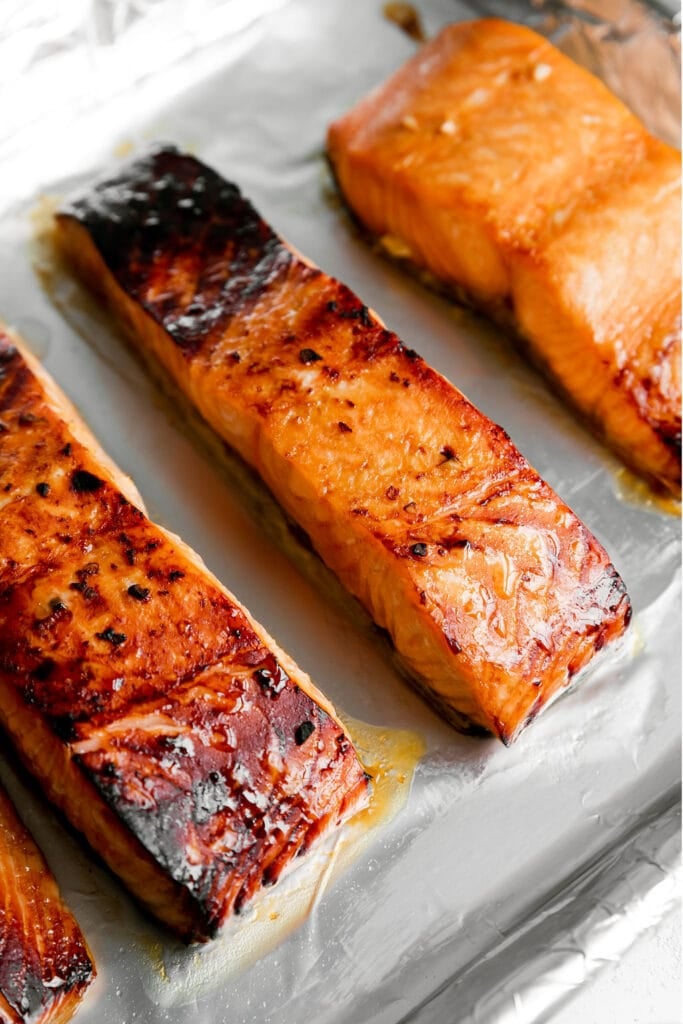 Four broiled teriyaki salmon filets on a foil covered sheet pan. 