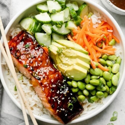 Overhead view white bowl filled with Teriyaki Salmon served over rice with veggies on side