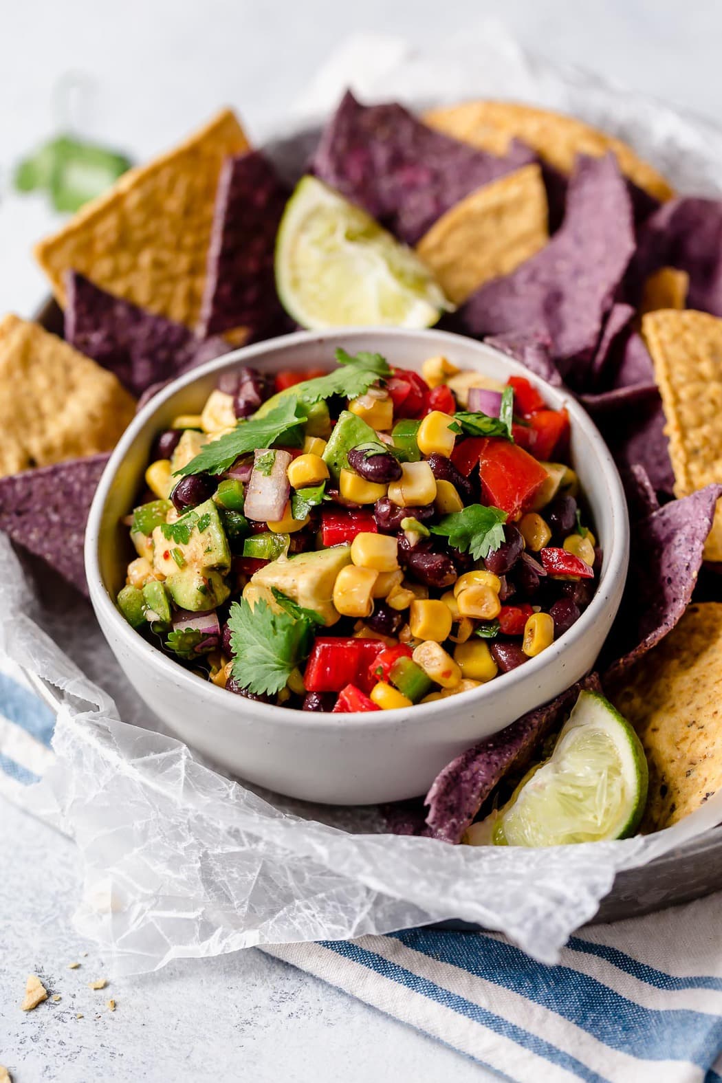 Black bean and corn salad in a white bowl with yellow and blue corn chips surrounding it.