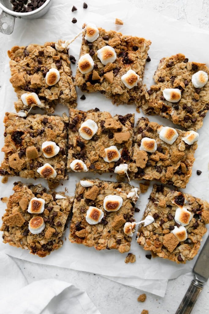 Overhead view of nine squares of chewy s'mores granola bars topped with toasted marshmallows on parchment paper