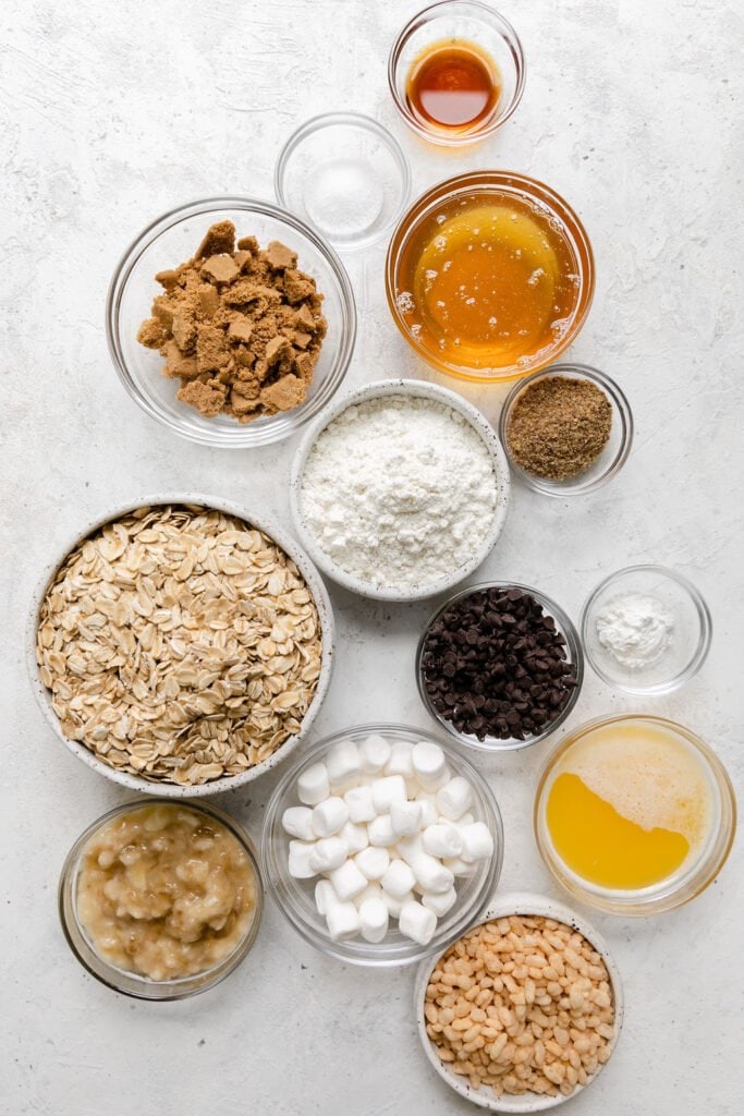 Overhead view of all ingredients for chewy s'mores granola bars arranged in small bowls. 
