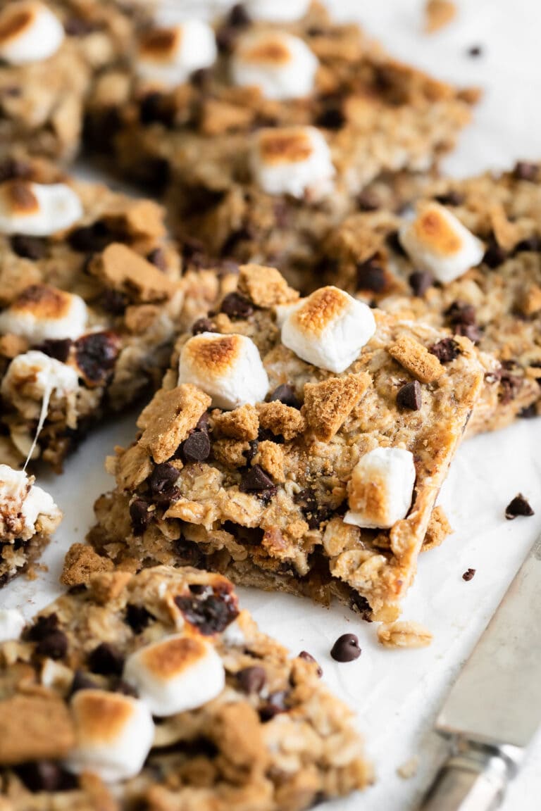 Close up view of square-cut chewy granola bar topped with toasted mini marshmallow perched on another square cut granola bar.
