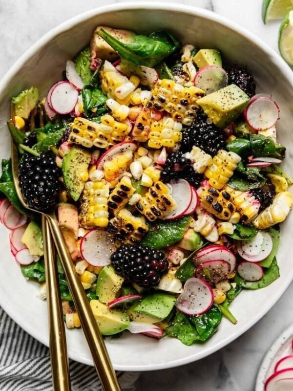 Overhead view grilled corn salad with blackberries in white bowl with gold cutlery.