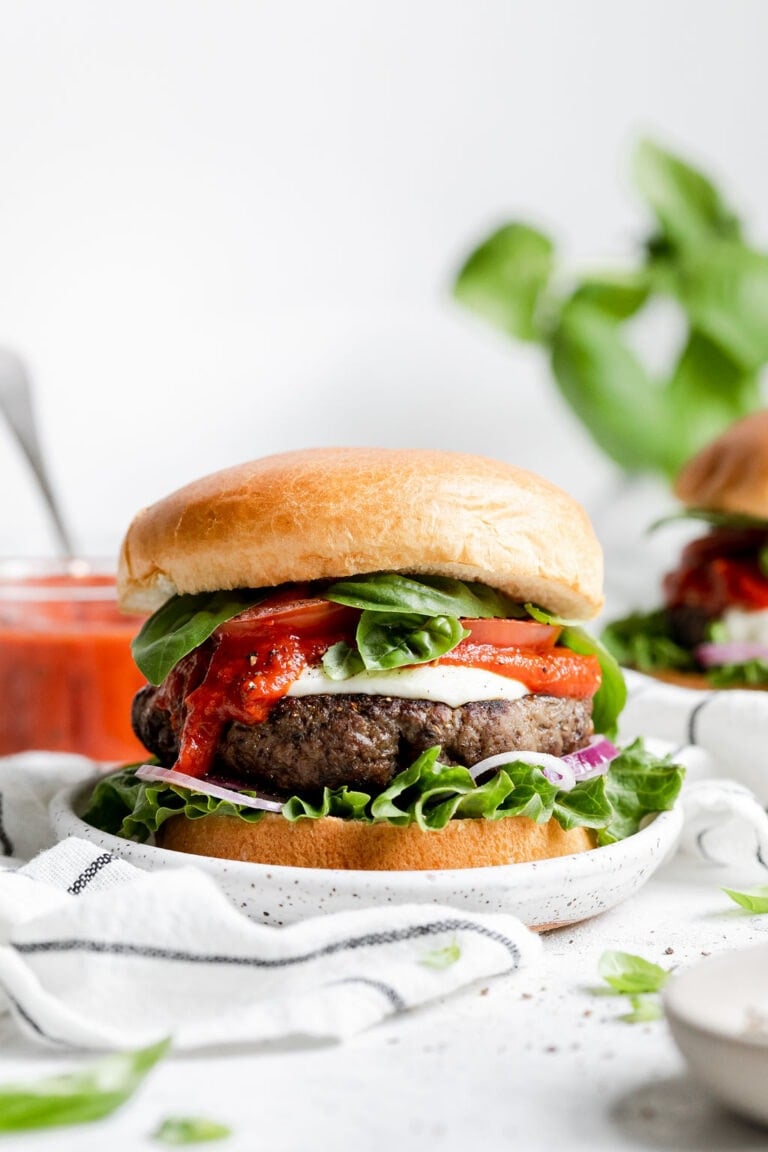 Side view of an Easy Grilled Pizza Burger on a bun topped with pizza sauce and fresh basil