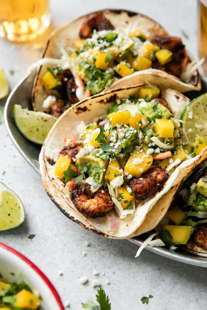 Close up view of a grilled shrimp taco in a double layered charred tortilla topped with mango avocado salsa and cojita cheese. 