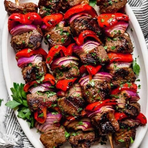 Overhead view of grilled steak kebabs on a white platter.