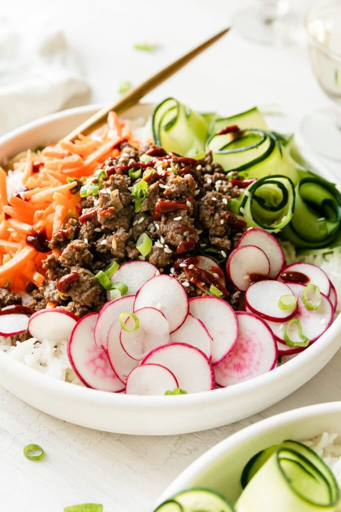 Close up view Korean-inspired ground beef bowl served over white rice topped with vegetables.
