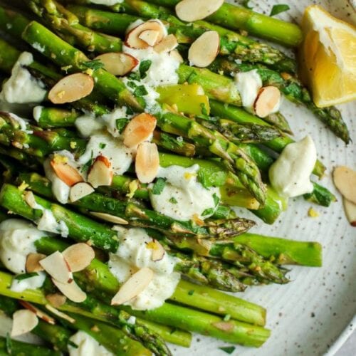 Close up side view of sautéed asparagus with goat cheese sauce served on plate with toasted almonds.