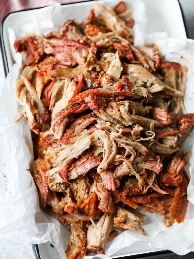 Smoked Pork Butt shredded on parchment-lined metal tray.