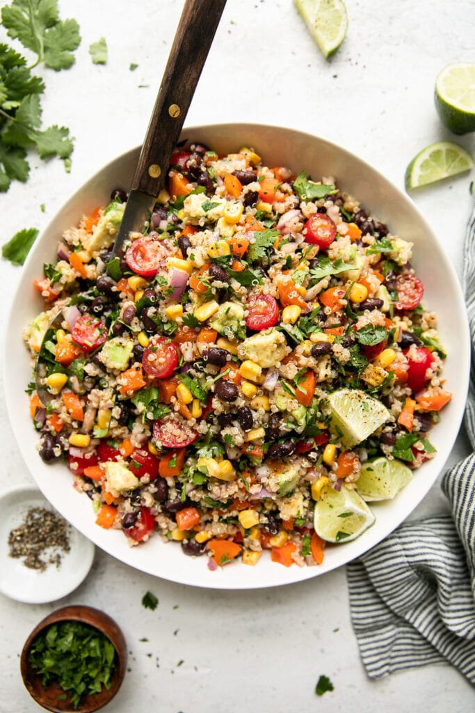 Overhead view Tex-Mex Quinoa salad with black beans and corn in a large white serving bowl with metal serving spoon.