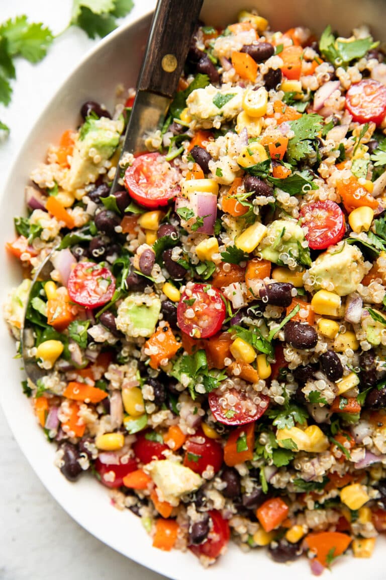 Overhead view of a serving bowl of Tex Mex quinoa salad topped with fresh herbs and colorful vegetables.
