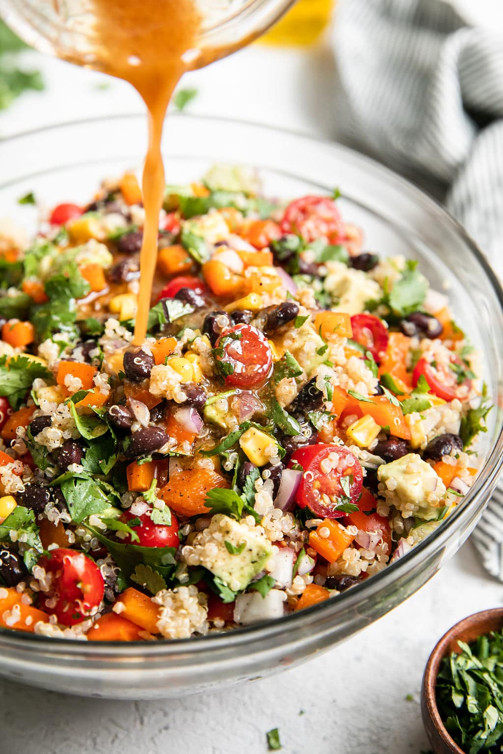 Tex-Mex Quinoa Salad with black beans and corn in clear glass mixing bowl with vinaigrette being poured over top.