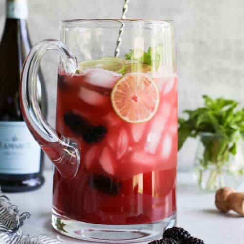 Large glass pitcher filled with blackberry lime prosecco cocktail.