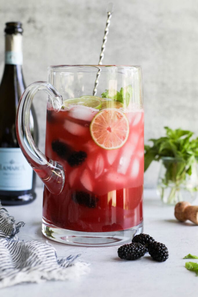 A large glass pitcher filled with blackberry lime prosecco cocktail