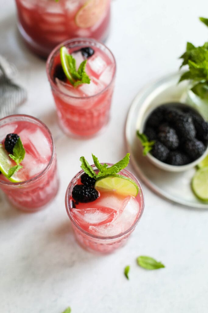 Blackberry lime prosecco cocktail served in three tall glasses with lime slices and fresh mint garnishing each drink. 