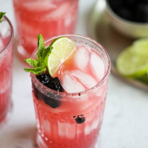 Tall glasses filled with blackberry lime prosecco cocktail garnished with lime slices and fresh mint.