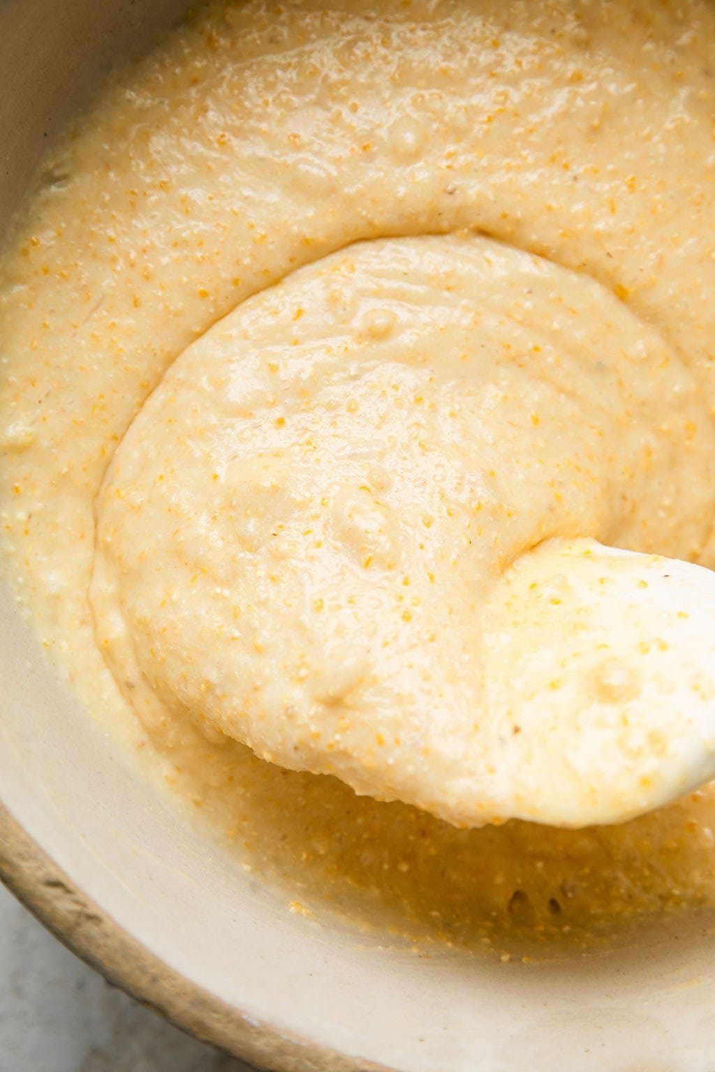 Close up view of a bowl of cornbread mixture ready to be poured into a muffin pan for baking.
