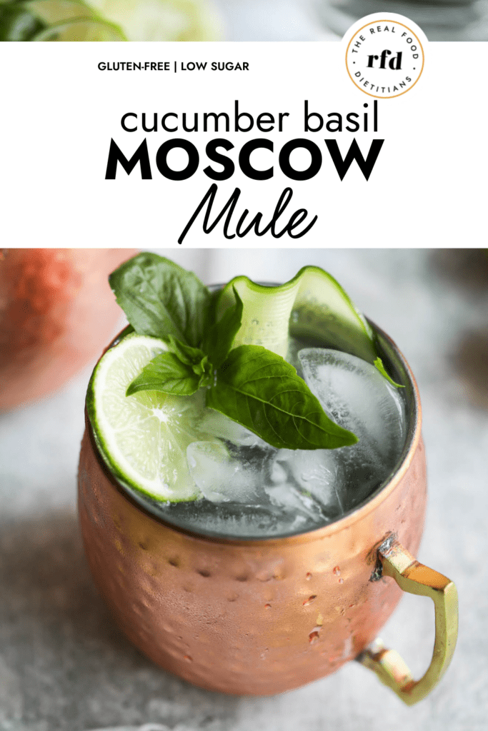 A copper cup filled with Cucumber Basil Moscow Mule garnished with lime slice, cucumber ribbon, and fresh basil.