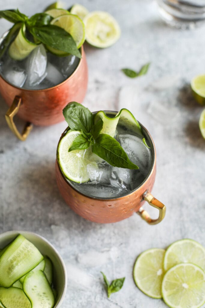 Overhead view copper cups filled with cucumber basil Moscow Mules garnished with lime slices and cucumber ribbons.