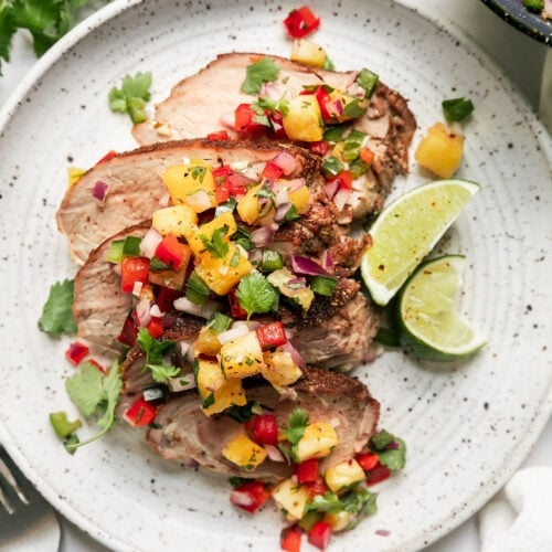 Overhead view grilled pork loin slices topped with pineapple salsa on plate.