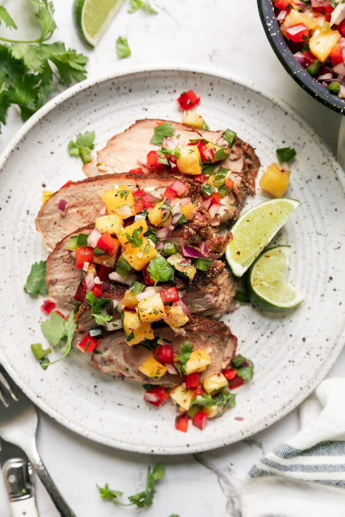 Overhead view round plate with serving of sliced grilled pork tenderloin topped with pineapple salsa 