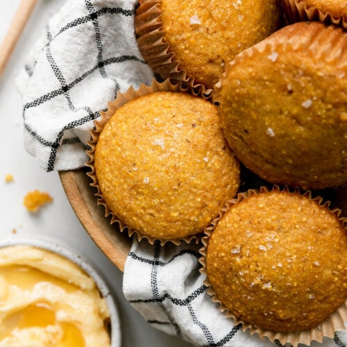 A dishtowel lined wooden bowl filled with homemade cornbread muffins.