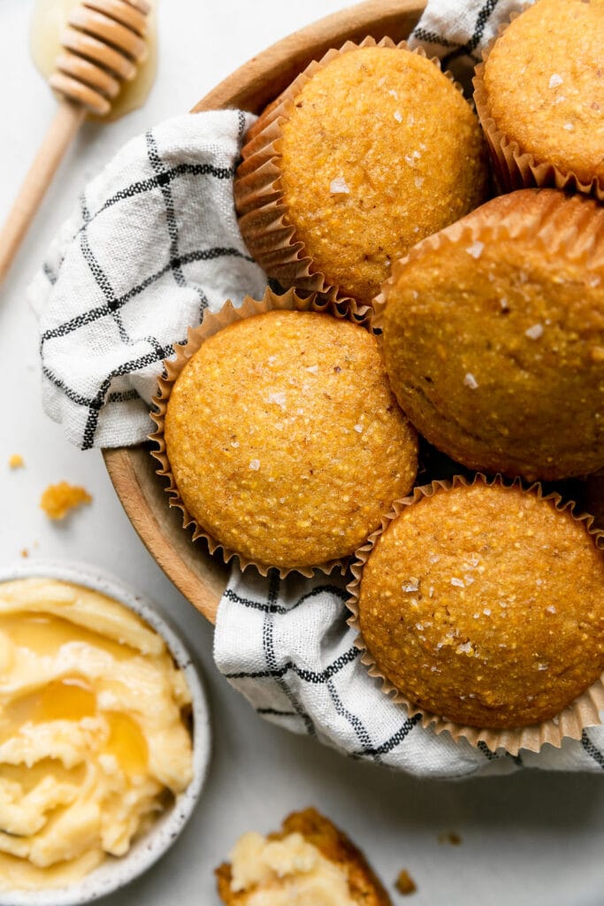 A small bowl filled with homemade cornbread muffins, bowl of honey butter to the side. 