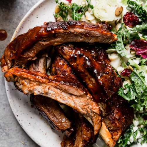 Instant pot baby back ribs with bbq sauce plated on white plate with sweet kale salad on side.