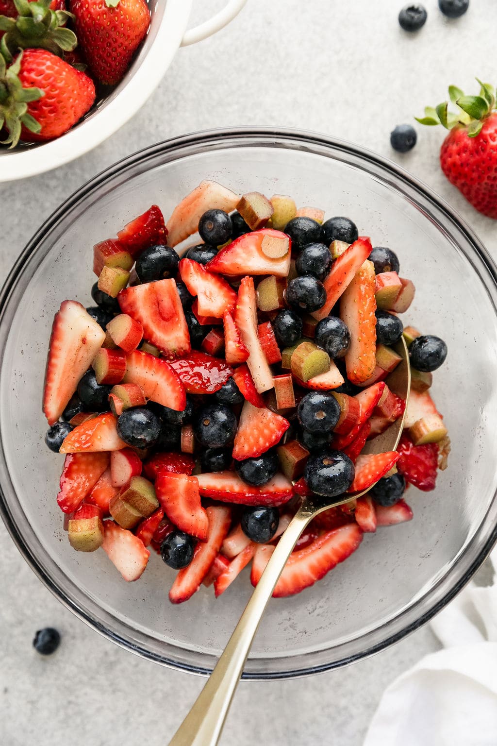 Galette filling of fresh sliced strawberries, blueberries, and rhubarb in clear glass mixing bowl.