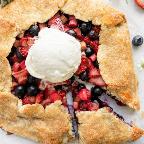 Overhead view strawberry blueberry galette with rhubarb on counter with one round scoop vanilla ice cream in middle of galette.