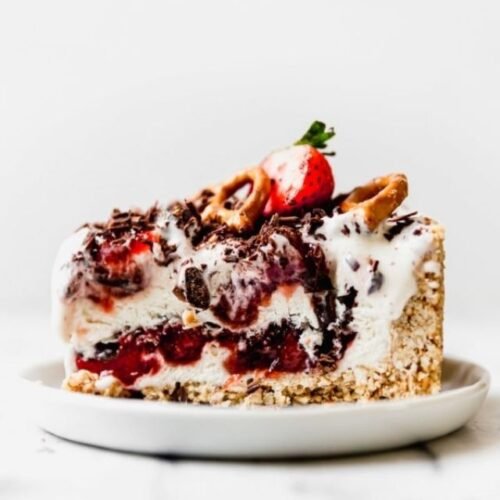 Side view of strawberry pretzel ice cream pie on white plate, topped with dark chocolate shavings