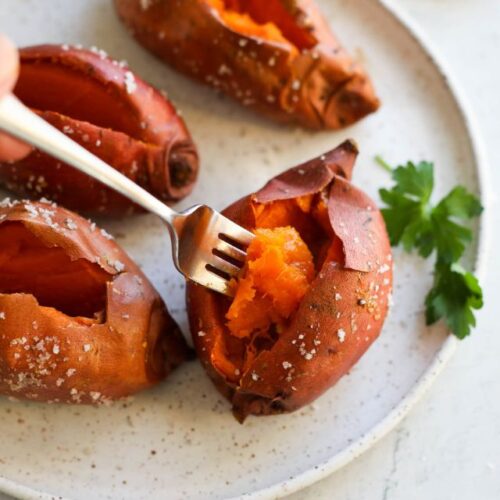 A forkful of fluffy sweet potato being removed from a baked sweet potato on a white plate.