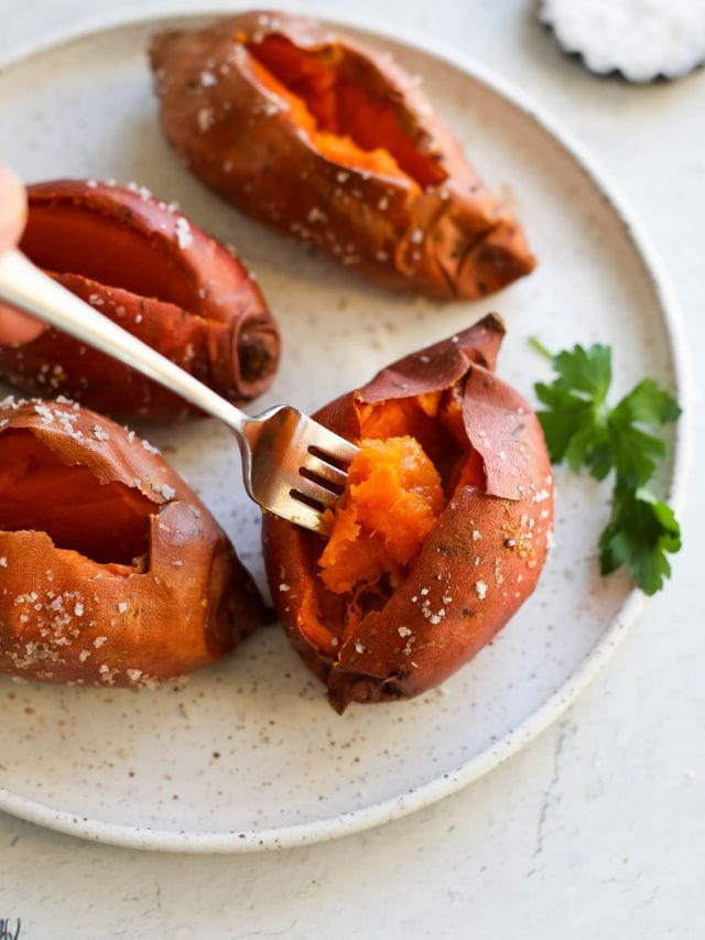 Baked sweet potatoes on stone plate with forkful lifting from one sweet potato