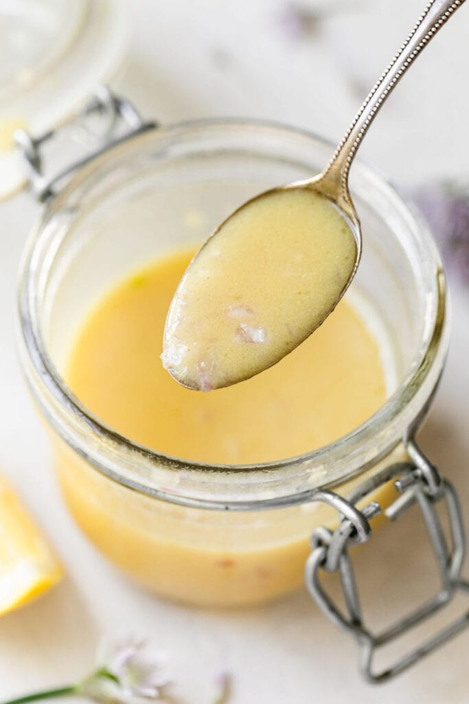 A spoonful of lemon dijon vinaigrette hovering over glass jar filled with dressing. 