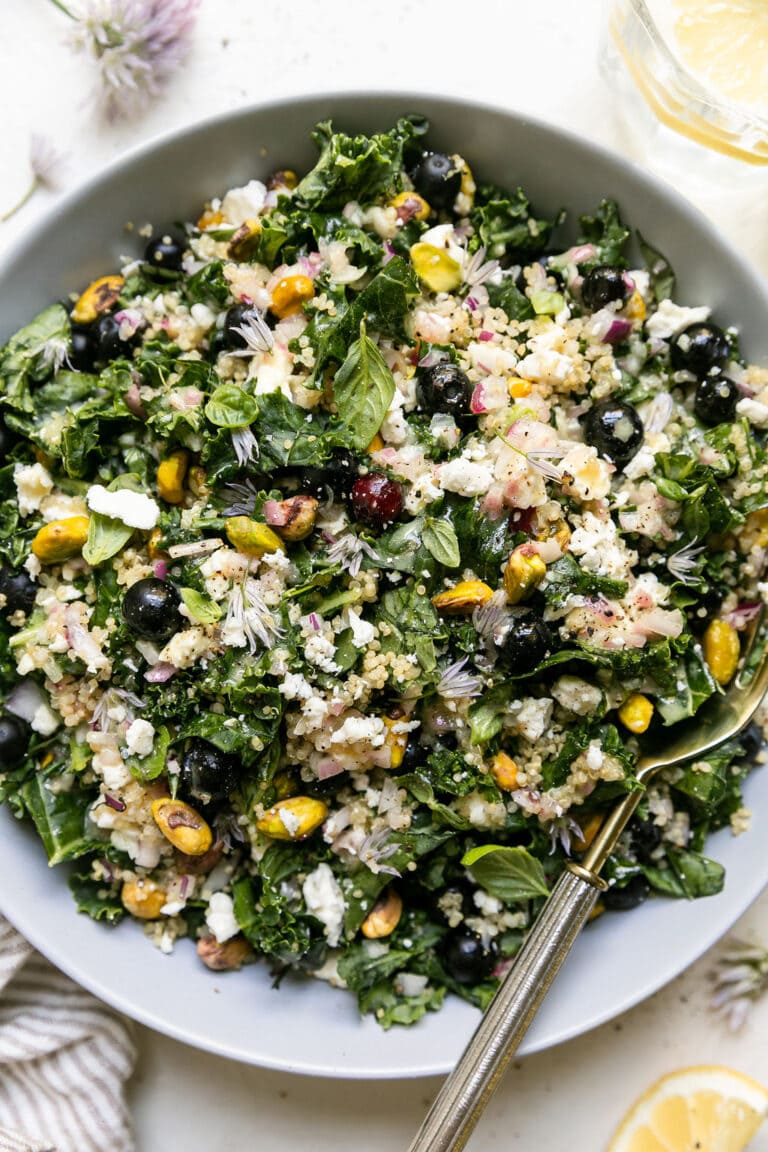 Overhead view Quinoa Kale Salad with fresh blueberries, pistachios and feta cheese, served in white bowl with serving spoon.