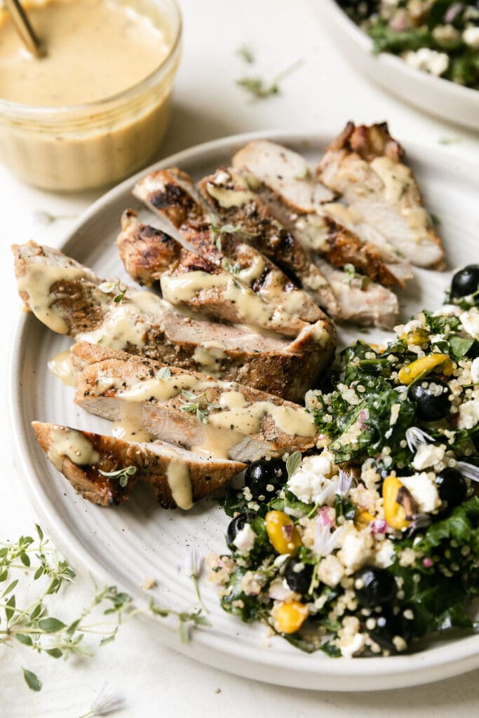 Grilled honey garlic pork chops cut into thick slices on plate with quinoa kale salad with blueberries on side. 