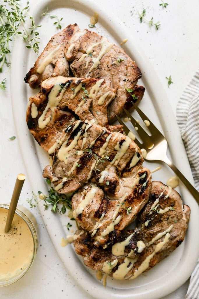 Grilled honey garlic pork chops on white platter drizzled with honey mustard sauce. 