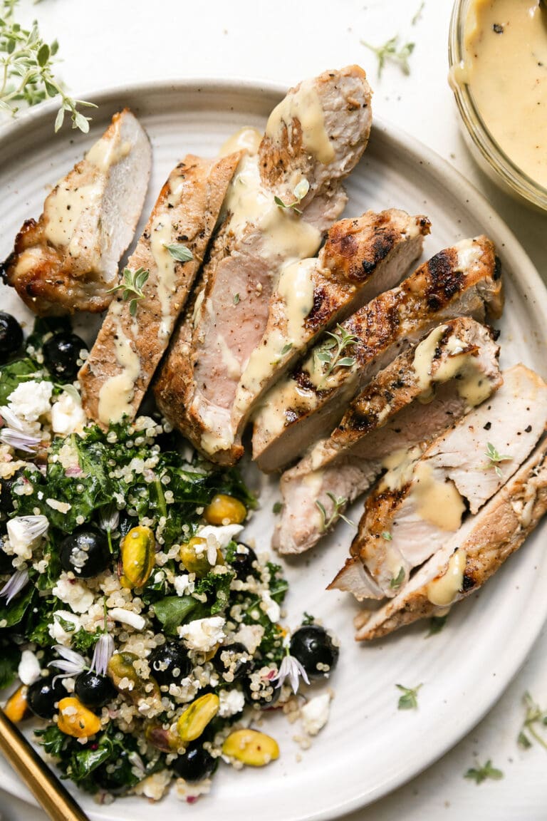 Overhead view of a plate of sliced grilled pork chops drizzled with honey garlic sauce and a side of blueberry quinoa salad. 