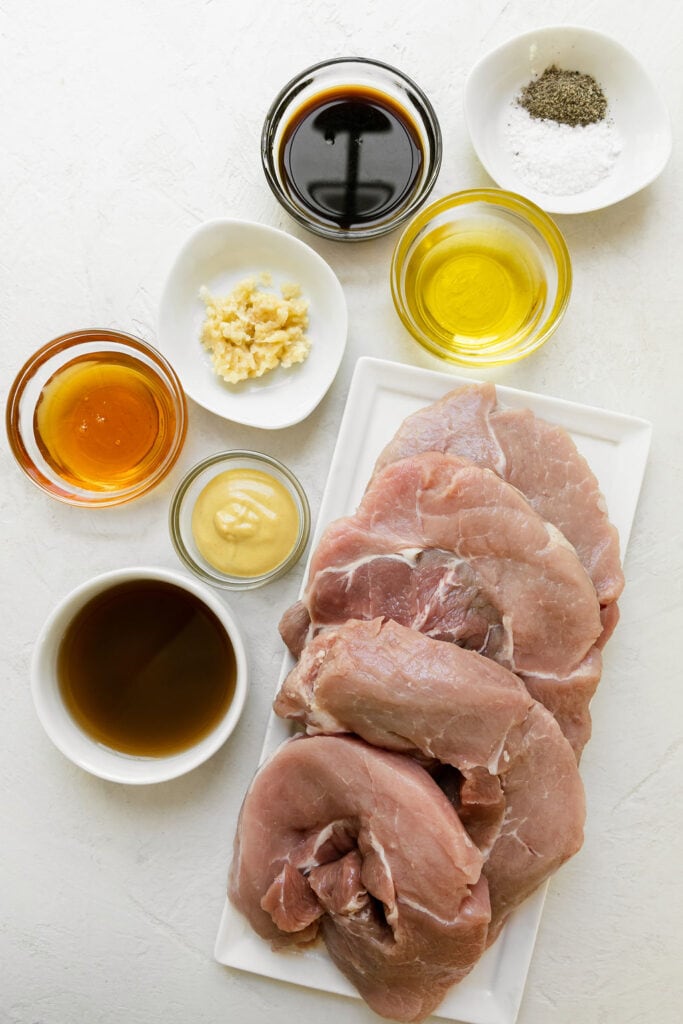 All ingredients for grilled honey garlic pork chops and honey mustard sauce in small bowls arranged together. 